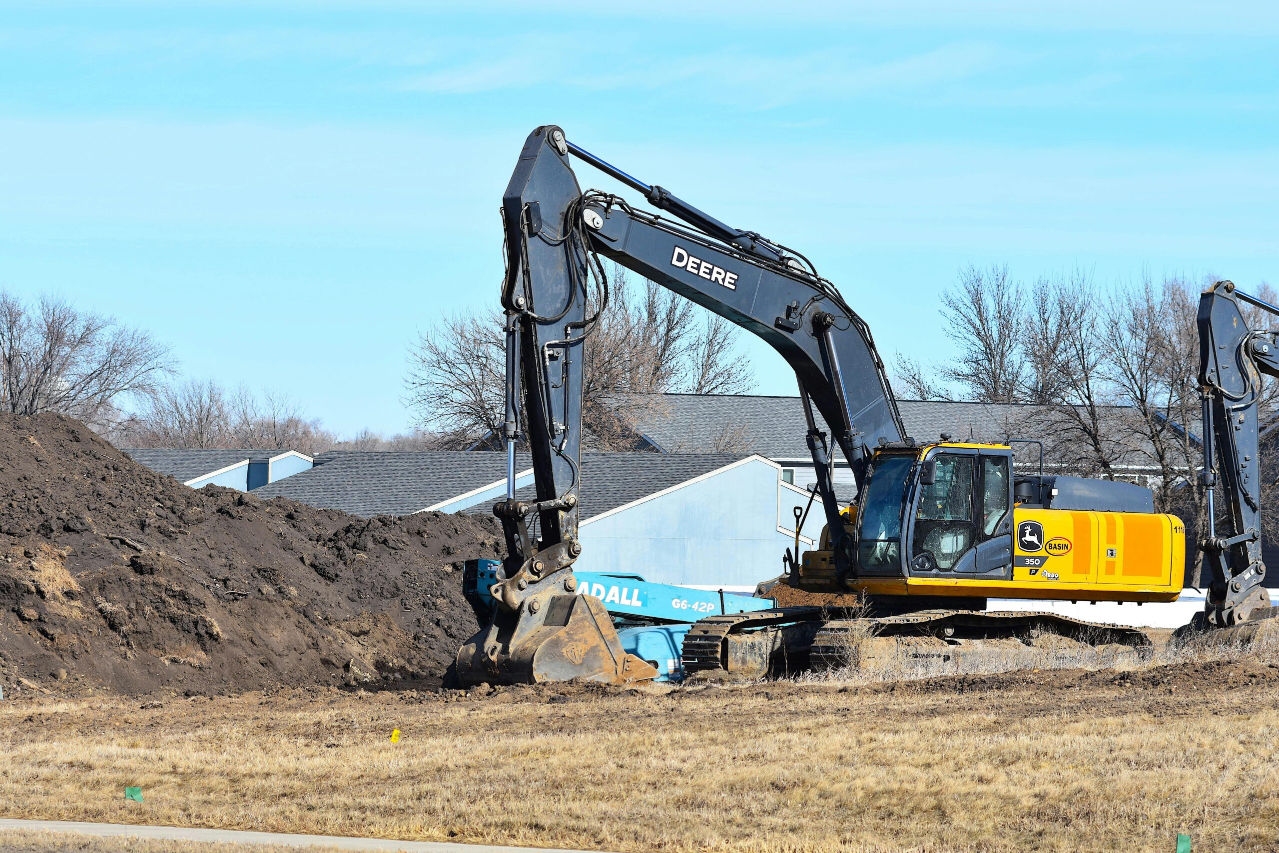 A yellow excavator moves dirt at a construction site under a clear blue sky.